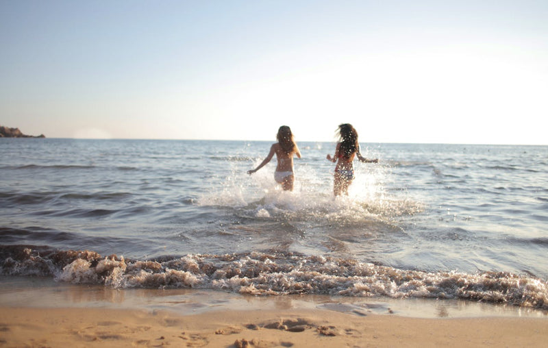 Dos mujeres en traje de baño corriendo hacia el mar